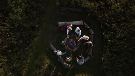Drone-Shot-Of-Mature-Friends-Making-Toast-As-They-Sit-Around-Fire-At-Outdoor-Campsite