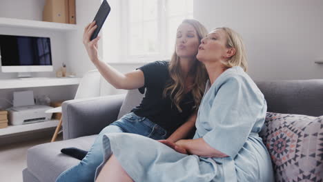 Senior-Mother-With-Adult-Daughter-Sitting-On-Sofa-Posing-For-Selfie-On-Mobile-Phone