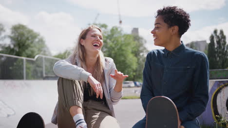 Two-Female-Friends-Talking-And-Laughing-In-Urban-Skate-Park