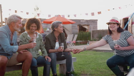 Group-Of-Mature-Friends-Sitting-Around-Fire-And-Drinking-At-Outdoor-Campsite-Bar
