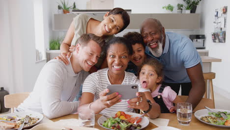 Familia-Multigeneracional-De-Raza-Mixta-Posando-Para-Selfie-Mientras-Comen-Juntos-Alrededor-De-La-Mesa-En-Casa
