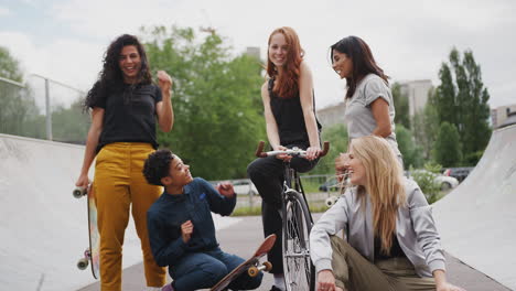 Portrait-Of-Female-Friends-With-Skateboards-And-Bike-Standing-In-Urban-Skate-Park