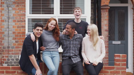 Outdoor-Portrait-Of-Student-Friends-Sitting-On-Wall-Outside-Shared-House-Together