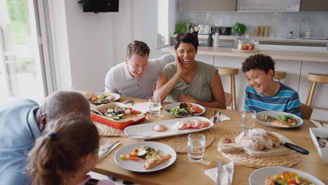 Multi-Generation-Mixed-Race-Family-Eating-Meal-Around-Table-At-Home-Together