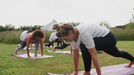 Female-Teacher-Leading-Group-Of-Mature-Men-And-Women-In-Class-At-Outdoor-Yoga-Retreat