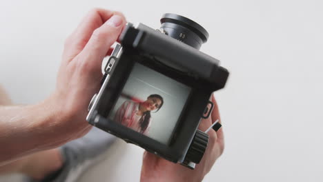 Photographer-Looking-Into-Viewfinder-Of-Vintage-Medium-Format-Camera-Taking-Portrait-Of-Young-Woman