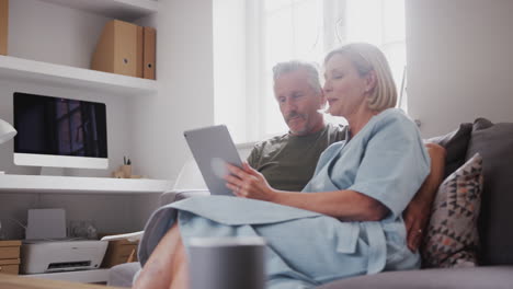 Älteres-Paar-Sitzt-Zu-Hause-Auf-Dem-Sofa-Und-Nutzt-Gemeinsam-Ein-Digitales-Tablet