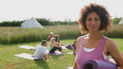 Portrait-Of-Mature-Woman-On-Outdoor-Yoga-Retreat-With-Friends-And-Campsite-In-Background