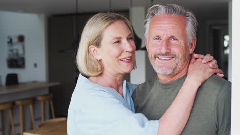 Portrait-Of-Loving-Senior-Couple-Standing-In-Kitchen-Together