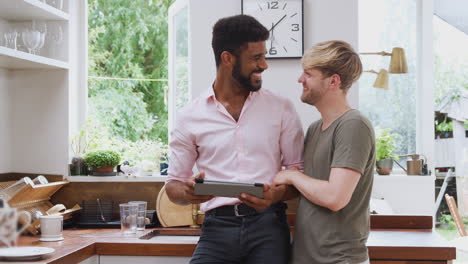 Male-Gay-Couple-Using-Digital-Tablet-At-Home-In-Kitchen-Together
