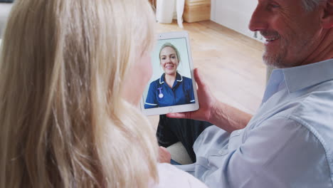 Älteres-Paar-Bei-Online-Beratung-Mit-Einer-Krankenschwester-Zu-Hause-Auf-Einem-Digitalen-Tablet