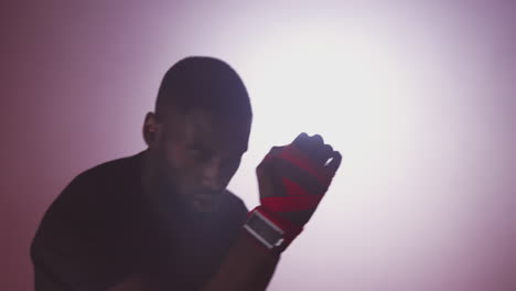 Dramatic-Backlit-Shot-Of-Male-Boxer-In-Gym-Wearing-Wraps-On-Hands-Training