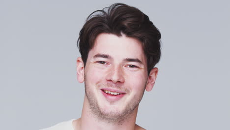 Head-And-Shoulders-Studio-Shot-Of-Young-Man-Smiling-At-Camera-In-Slow-Motion