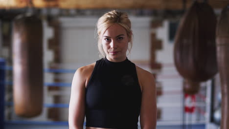 Portrait-Of-Female-Boxer-In-Gym-Training-With-Old-Fashioned-Punching-Bags