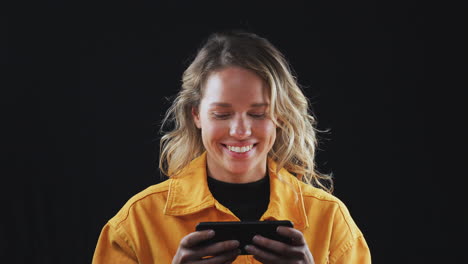 Studio-Shot-Of-Woman-Streaming-Content-On-Mobile-Phone-And-Smiling-In-Slow-Motion