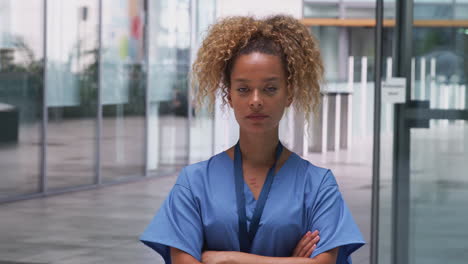 Portrait-Of-Female-Nurse-Wearing-Scrubs-Standing-In-Modern-Hospital-Building