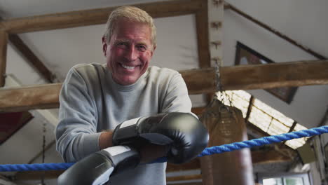 Portrait-Of-Senior-Male-Boxing-Coach-In-Gym-Standing-In-Boxing-Ring