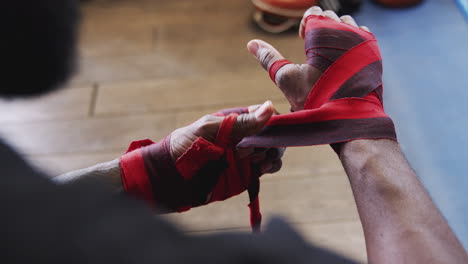 Close-Up-Of-Male-Boxer-Training-In-Gym-Putting-Wraps-On-Hands-Standing-Next-To-Punching-Bag