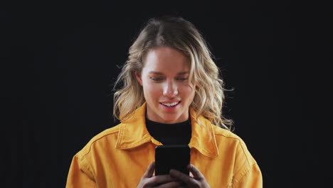 Studio-Shot-Of-Woman-Streaming-Content-On-Mobile-Phone-And-Smiling-In-Slow-Motion