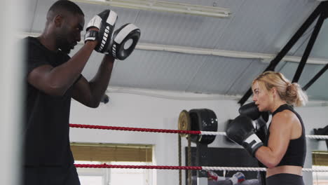Male-Boxing-Coach-With-Female-Boxer-In-Gym-Using-Training-Gloves-Sparring-In-Ring