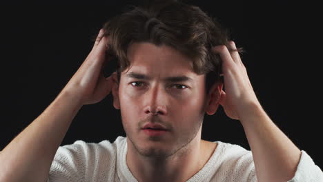 Head-And-Shoulders-Studio-Shot-Of-Unhappy-Man-Looking-Playing-With-Hair-In-Slow-Motion