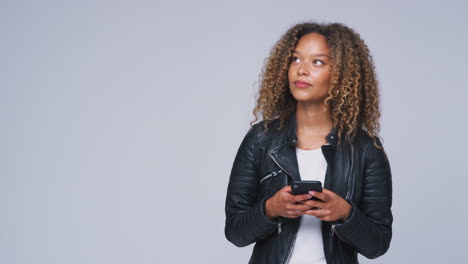 Studio-Shot-Of-Woman-Wearing-Leather-Jacket-Sending-Text-Message-On-Mobile-Phone-In-Slow-Motion