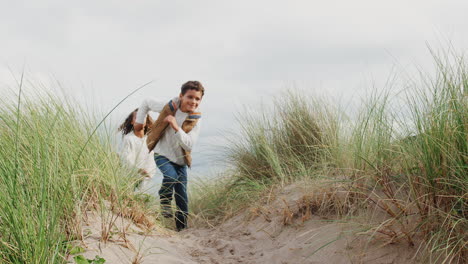 Children-Chasing-Dog-Running-Through-Sand-Dunes-On-Winter-Beach-Vacation