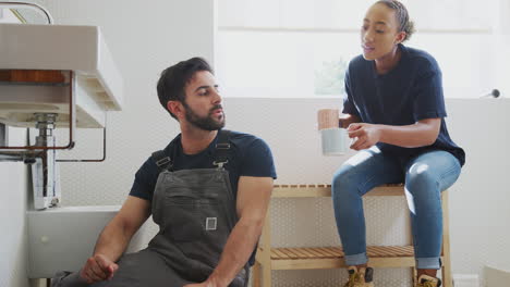 Male-Plumber-With-Female-Apprentice-Taking-A-Break-From-Fixing-Leaking-Sink-In-Home-Bathroom