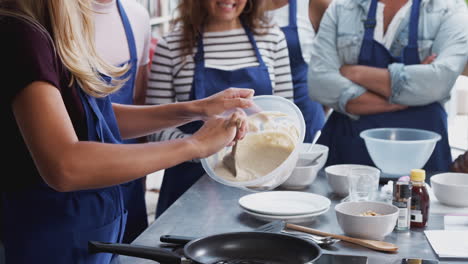 Close-Up-Of-Female-Teacher-Adding-Mixture-To-Pan-In-Cookery-Class