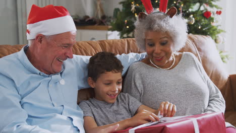 Aufgeregt-Sitzt-Der-Enkel-Mit-Den-Großeltern-Auf-Dem-Sofa-Und-öffnet-Geschenke-Am-Weihnachtstag