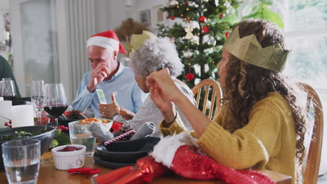 Mehrgenerationenfamilie-Spielt-Mit-Weihnachtscracker-Neuheiten,-Während-Sie-Zum-Essen-Am-Tisch-Sitzt