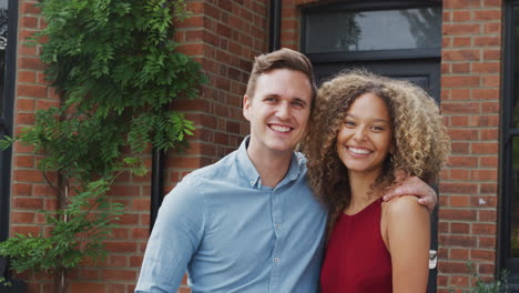 Portrait-Of-Excited-Young-Couple-Standing-Outside-New-Home-Together
