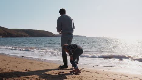 Father-And-Son-Walking-Along-Beach-By-Breaking-Waves-On-Beach-Collecting-Stones-To-Skim