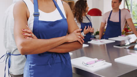 Close-Up-Of-Woman-Wearing-Apron-Folding-Arms-Taking-Part-In-Cookery-Class-In-Kitchen