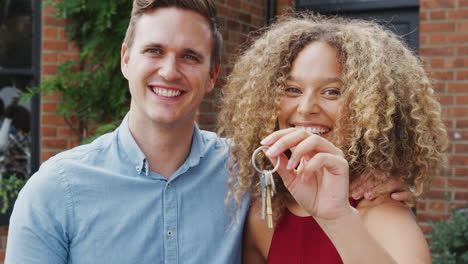 Portrait-Of-Excited-Young-Couple-Standing-Outside-New-Home-Holding-Keys-Together