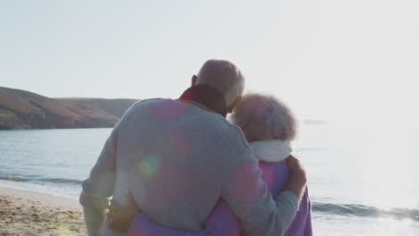 Rückansicht-Eines-Liebevollen,-Aktiven-Seniorenpaares,-Das-Im-Winterurlaub-Am-Strand-Entlang-Der-Küste-Spaziert