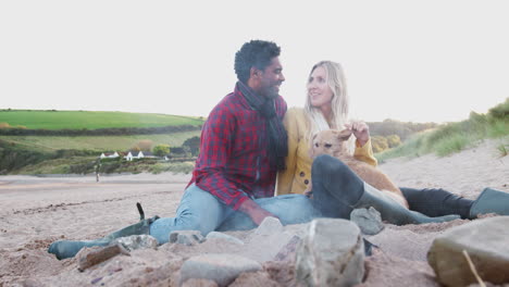 Loving-Couple-With-Dog-Relaxing-By-Fire-On-Winter-Beach-Vacation