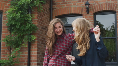Portrait-Of-Excited-Gay-Female-Couple-Standing-Outside-New-Home-Holding-Keys-Together