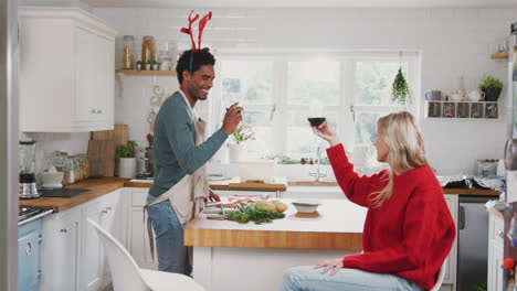 Couple-Wearing-Fancy-Dress-Antlers-Making-A-Toast-Whilst-Preparing-Dinner-On-Christmas-Day