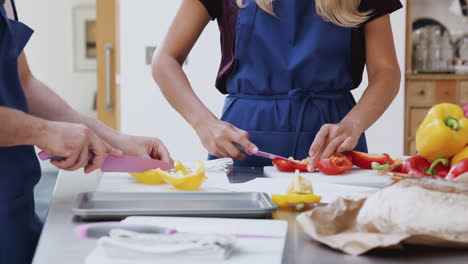 Male-And-Female-Adult-Students-Chopping-Peppers-For-Dish-In-Kitchen-Cookery-Class