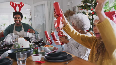 Mehrgenerationenfamilie-Zieht-Weihnachtscracker,-Während-Sie-Zum-Essen-Am-Tisch-Sitzt