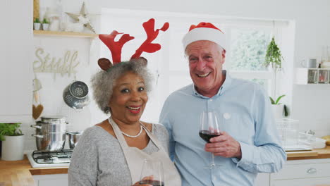 Portrait-Of-Senior-Couple-Wearing-Fancy-Dress-Antlers-Making-A-Toast-Whilst-Preparing-Dinner-On-Christmas-Day