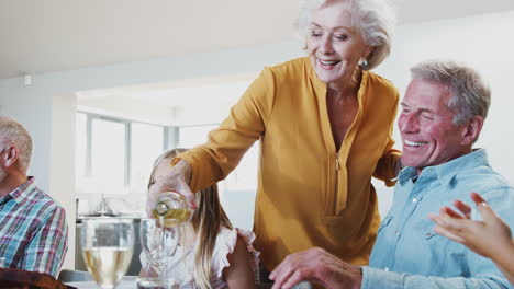 Grandmother-Pouring-Wine-As-Multi-Generation-Family-Meet-For-Meal-At-Home