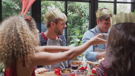 Group-Of-Friends-Sitting-Around-Dining-Table-At-Home-Enjoying-Christmas-Dinner-Together