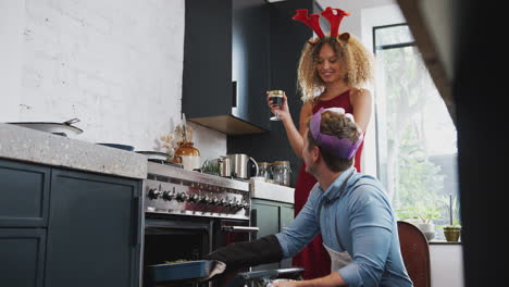 Pareja-Vistiendo-Disfraces-De-Astas-Y-Sombrero-De-Papel-En-Casa-Cocinando-Una-Cena-Vegetariana-El-Día-De-Navidad