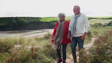 Active-Senior-Couple-Holding-Hands-As-They-Walk-Along-Coastal-Path-In-Fall-Together