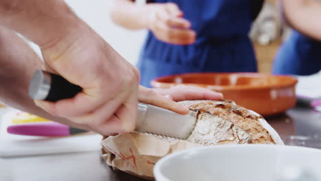 Close-Up-Of-Man-Slicing-Bread-For-Dish-In-Kitchen-Cookery-Class