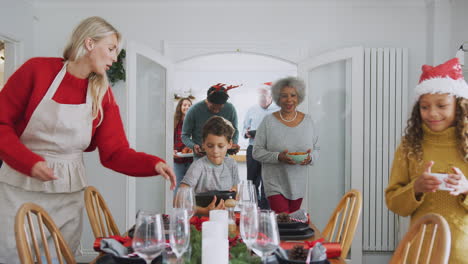Multi-Generation-Family-Bringing-Food-Into-Dining-Room-For-Christmas-Meal