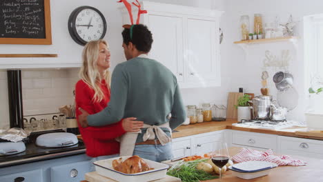 Loving-Couple-Wearing-Fancy-Dress-Antlers-Dancing-In-Kitchen-Whilst-Preparing-Christmas-Dinner