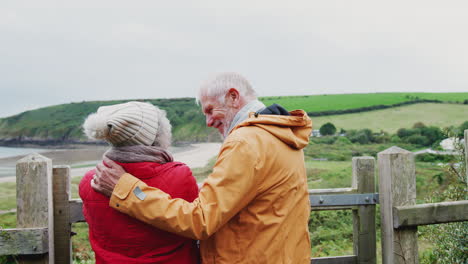 Rear-View-Of-Active-Senior-Couple-Looking-Out-Over-Gate-As-They-Walk-Along-Coastal-Path-In-Fall